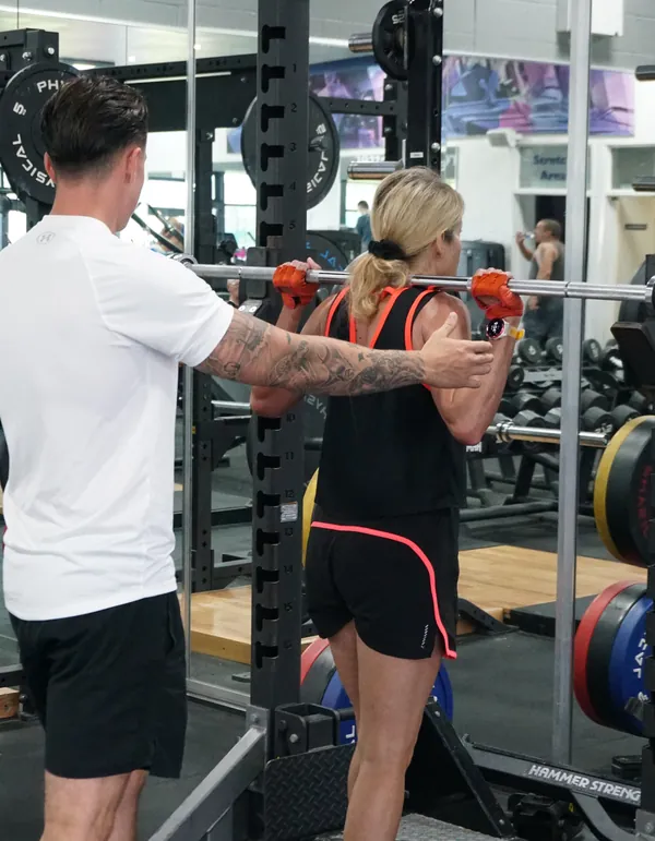 Lukas Kettle adjusting a client’s shoulder position under the bar in the squat rack