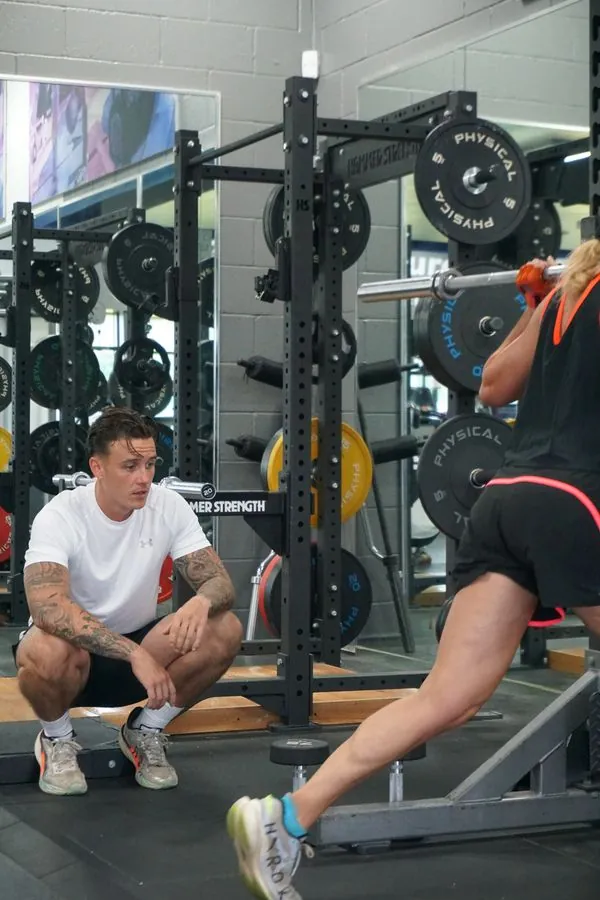 Lukas Kettle watching a client’s form during a barbell back squat in the squat rack